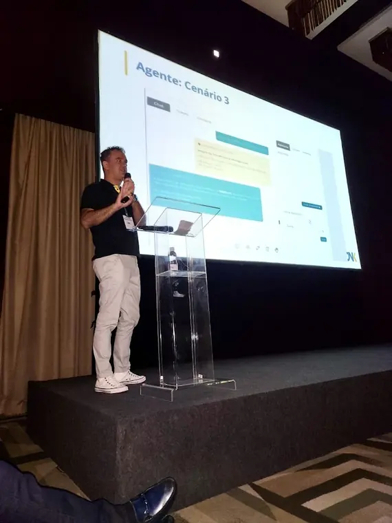 Fabricio Costa palestrando sobre agentes de inteligência artificial, com um cenário de agente projetado na tela