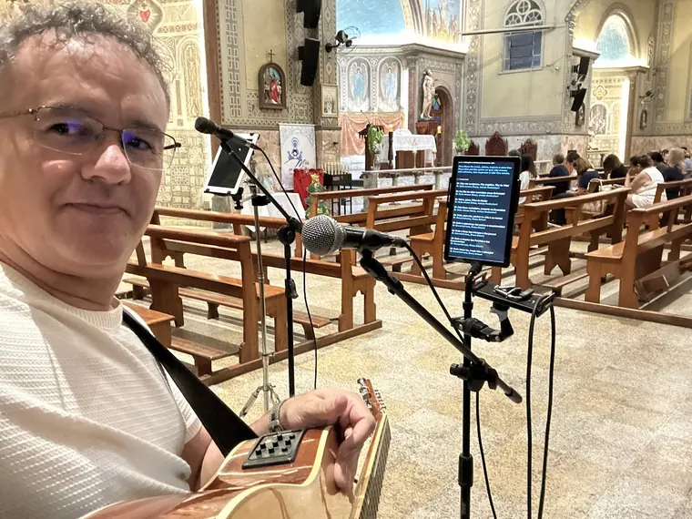 Fabricio Costa tocando violão na igreja, diante dos microfones
